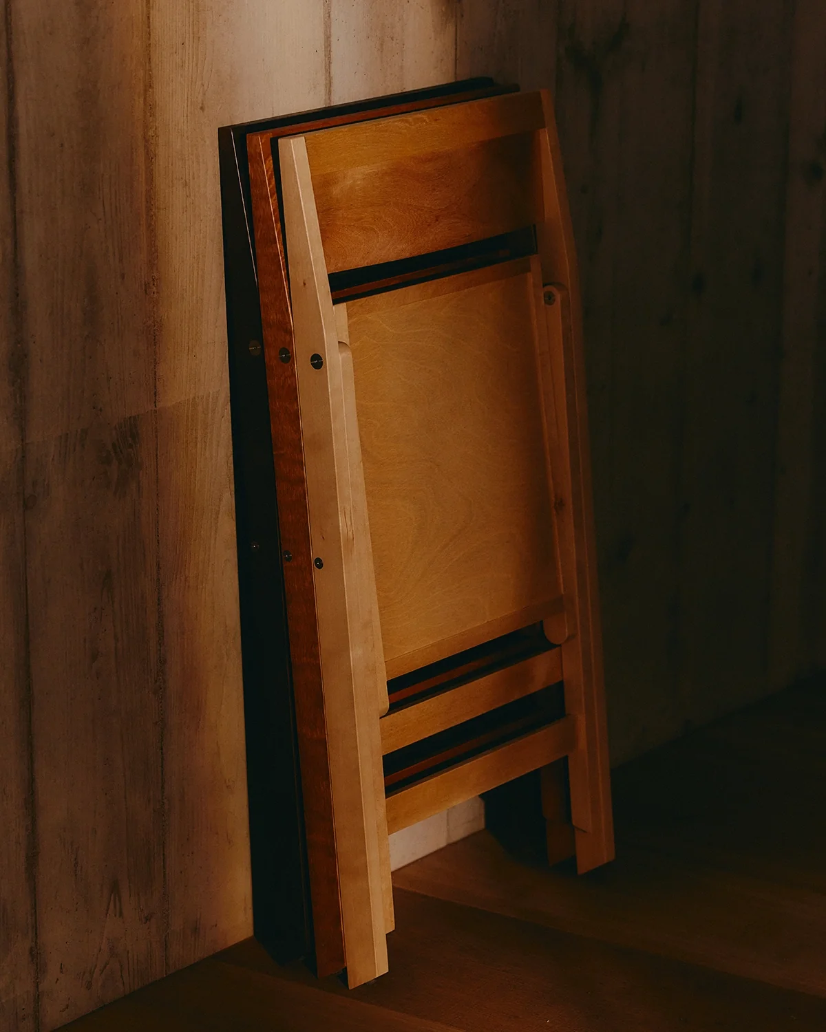 Folded wooden chairs leaning against a timber wall