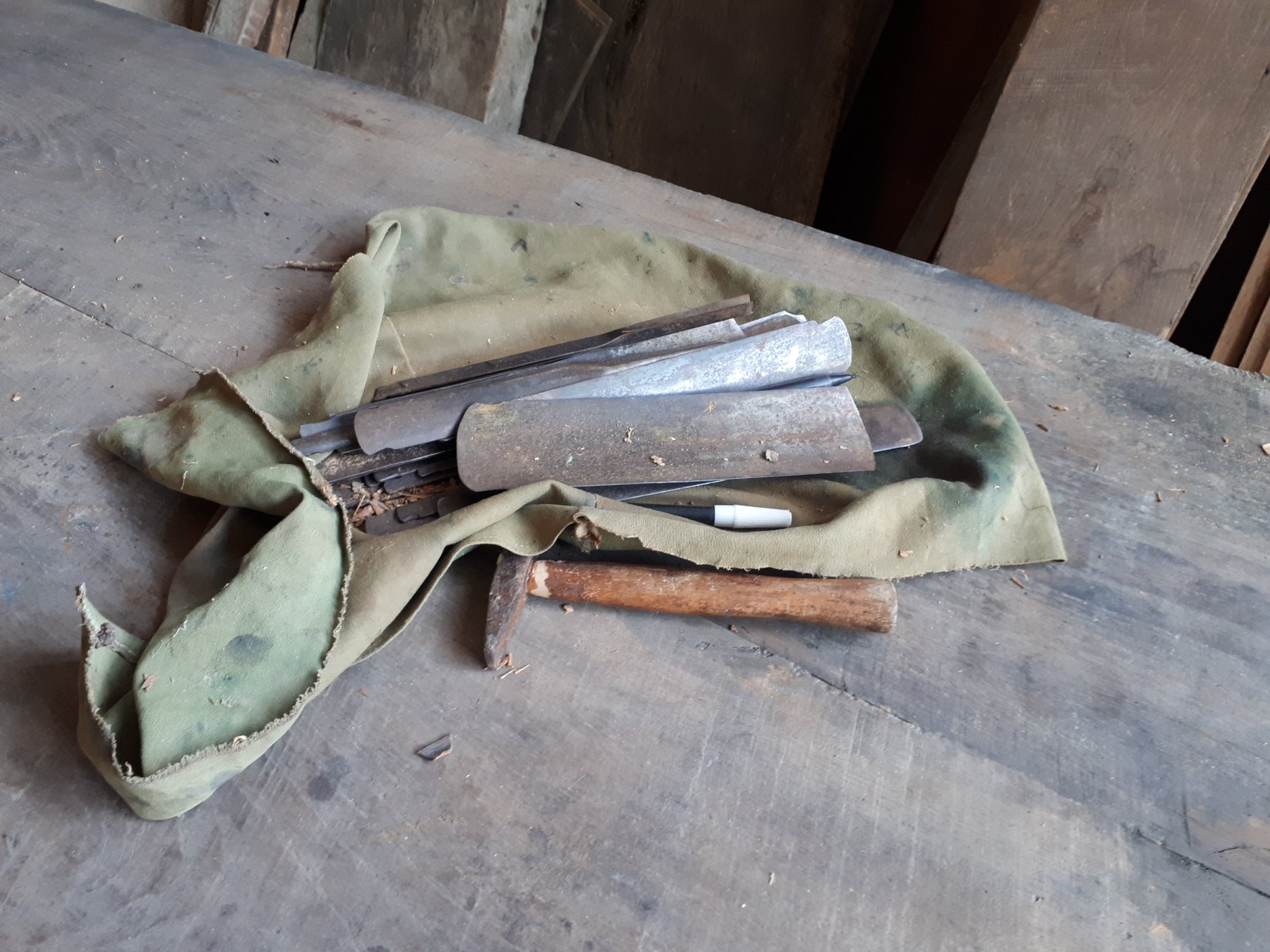 Steel scrapers and a hammer wrapped in a green cloth on a worn wooden workbench